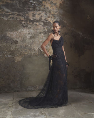 Slight side view of the Lace Minerva gown in black, showcasing the twisted asymmetric neckline and graceful lines of the gown.