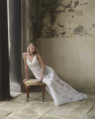 Front view of the Lace Minerva gown in white, with the model laid to the side, accentuating the gown's luxurious flow and design.
