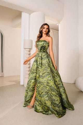 Woman wearing a green strapless gown with a slit in a white room.