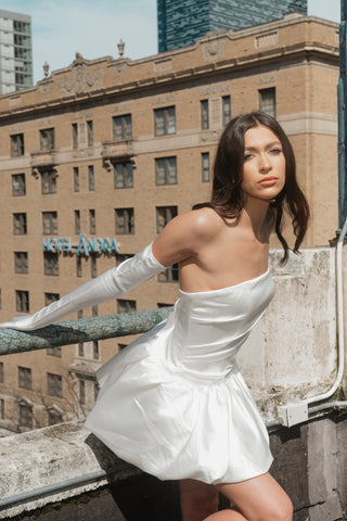 Fitted satin mini dress featuring a sculpted strapless neckline and dramatic peplum detailing