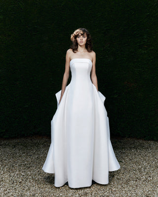 Modern wedding dress with a sleek strapless neckline, structured column silhouette, and dramatic Victorian-inspired bustle.