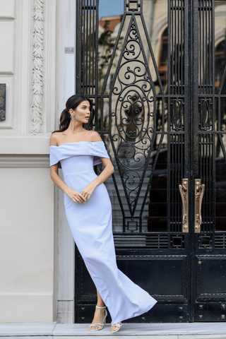 Model wearing the full-length Lucia Bardot gown by Nadia’s, featuring a floral neckline, fitted crepe silhouette, and elegant column skirt with a back slit.