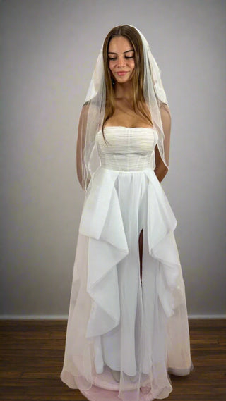 Woman wearing a white wedding dress with a veil against a plain background
