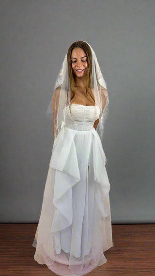 Woman wearing a white wedding dress with a veil against a gray background