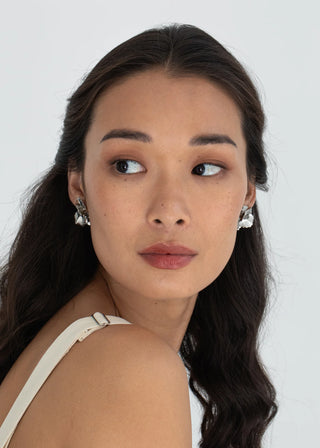 Woman with long dark hair wearing white earrings against a plain background