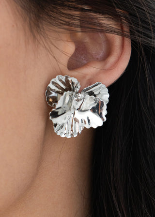 Silver floral earring worn by a person with dark hair.
