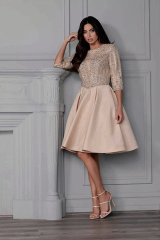 Woman wearing a beige dress with lace top against a gray wall.