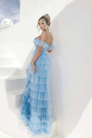Woman in a blue tiered dress standing on white steps with a white building in the background