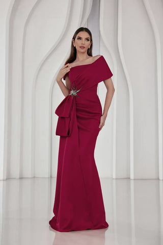 Woman wearing a burgundy one-shoulder dress with a brooch against a white background