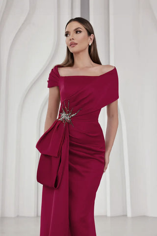 Woman wearing a burgundy off-shoulder dress with a floral detail against a white background