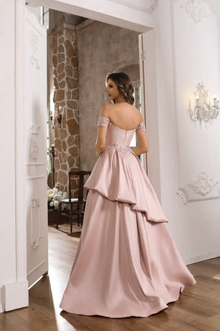 Woman in a pink evening gown standing in a room with stone walls and wooden floors.
