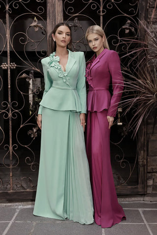 Two women in elegant dresses standing in front of an ornate metal gate.