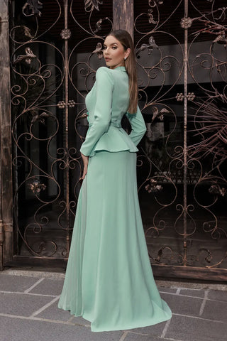 Woman in a mint green outfit standing in front of an ornate metal gate.