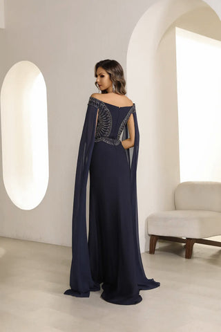 Woman wearing a navy blue evening gown with a cape in a modern interior setting.