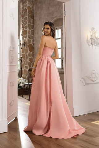 Woman in a pink strapless gown standing in a room with stone walls and wooden floors.