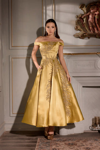 Woman wearing a gold off-shoulder gown in an elegant room.