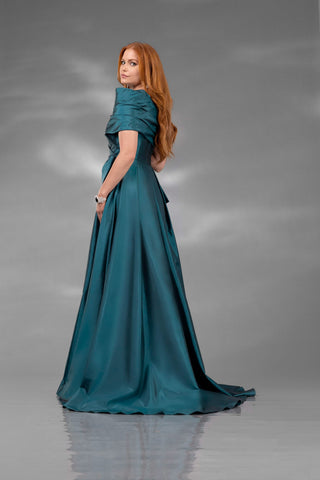 Woman in a teal evening gown standing against a gray background