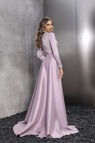 Woman in a long, light purple dress standing against a gray wall.