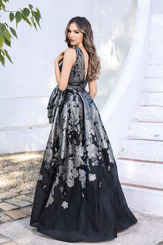 Woman in a black floral evening gown standing outdoors with a white background