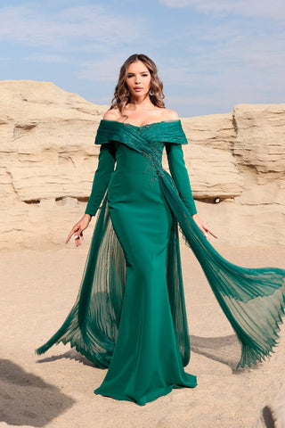 Woman in a green off-shoulder gown standing against a rocky landscape.