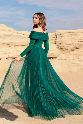 Woman in a green off-shoulder dress standing against a rocky landscape.
