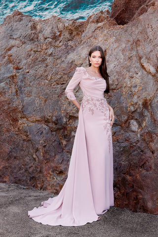 Woman in a pink evening gown standing against a rocky coastal background