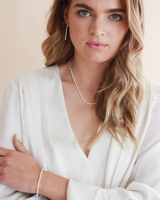 Woman wearing a white top and pearl necklace against a neutral background