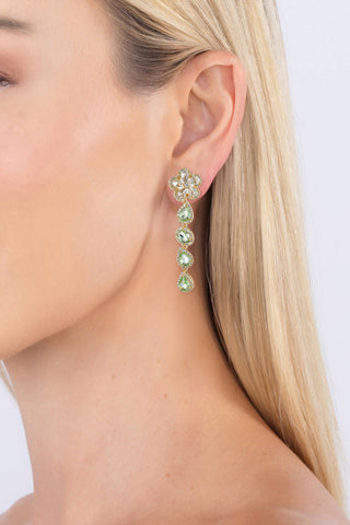 Close-up of a woman wearing a floral earring with green gemstones on a white background