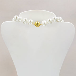 Pearl necklace with a gold bead on a white stand against a light background