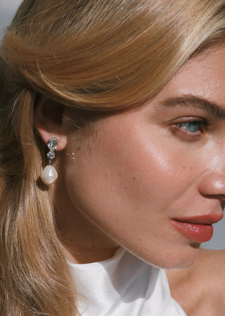 Close-up of a woman wearing pearl and crystal earrings with a blurred background
