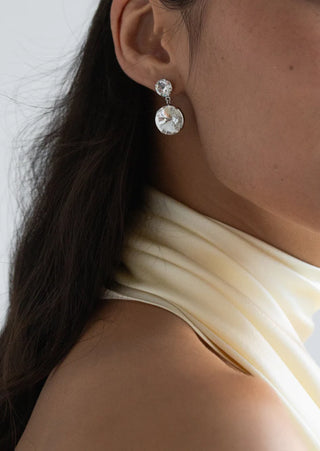 Close-up of a person wearing silver earrings with a plain background