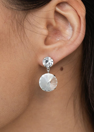 Close-up of an ear wearing a silver earring with a clear gemstone.