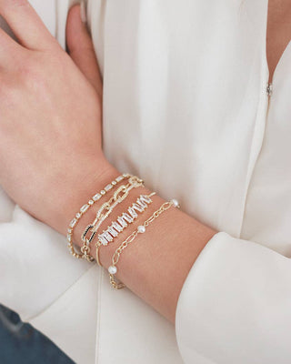 Gold bracelets with pearls on a person's wrist against a white background