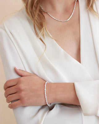 Person wearing a pearl bracelet and necklace on a plain background