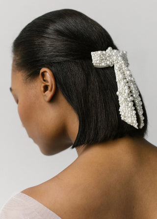 Model showcasing the Donna Bow Barrette in a side view with hair down, highlighting the pearl embroidery.