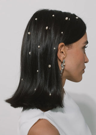 Woman with pearl hairpins in her black hair against a plain background