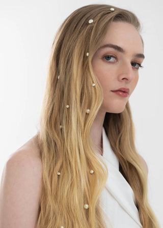 Woman with long blonde hair featuring pearl hair accessories against a white background