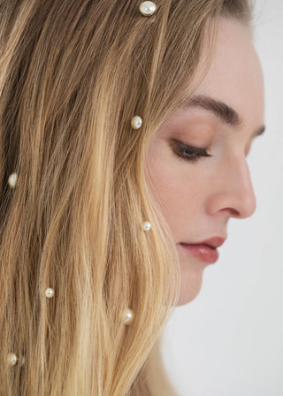 Close-up of a woman's face with pearl hairpins in her blonde hair against a white background