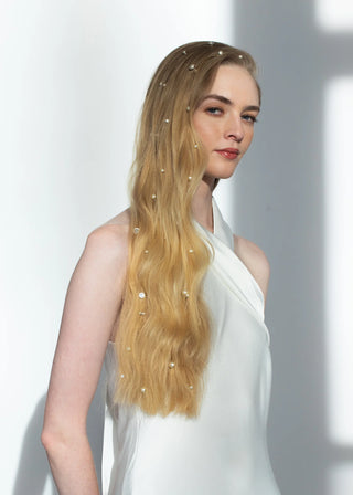 Woman with long blonde hair adorned with small decorative elements against a plain background