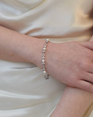 Pearl bracelet on a wrist against a white satin background