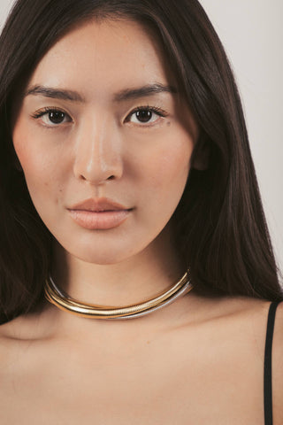 Woman wearing a gold choker necklace against a plain background