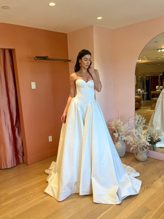 Woman in a white wedding dress standing in a room with pink walls and wooden floor.