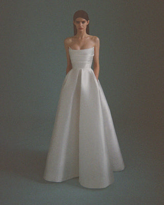 Model wearing a strapless ivory silk bridal ball gown with a corsetted bodice and pleated full-length skirt.”