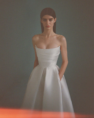 Model in a strapless ivory silk bridal gown with a pleated waist and concealed pockets, showcasing a fitted bodice.