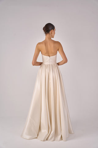 Woman wearing a strapless, floor-length beige gown on a plain background