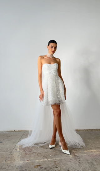 Woman wearing a strapless white wedding dress with a long train against a plain background