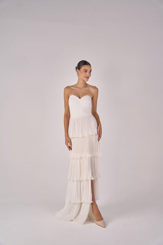 Woman wearing a strapless, tiered white dress on a plain background