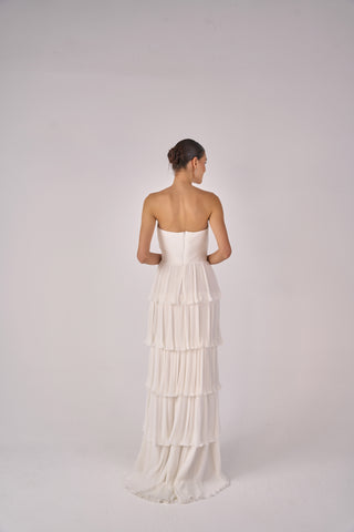 Woman wearing a strapless, tiered white dress on a plain background