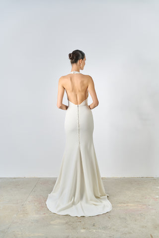 Woman wearing a white gown with an open back against a plain white background