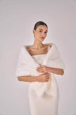 Woman wearing a white fur shrug over a plain background